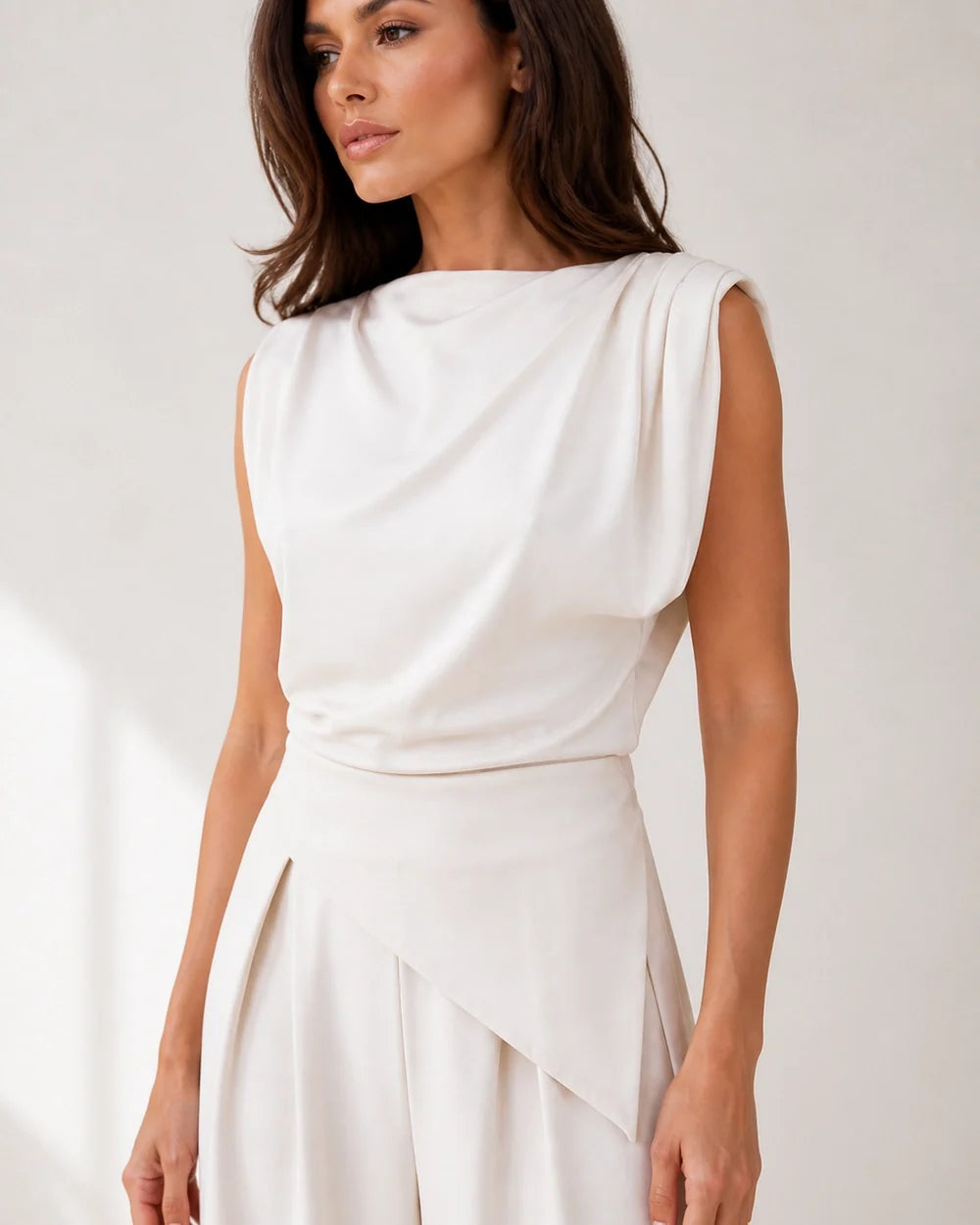 Women's white asymmetric draped top and wide-leg trousers set, drape and waist detail.